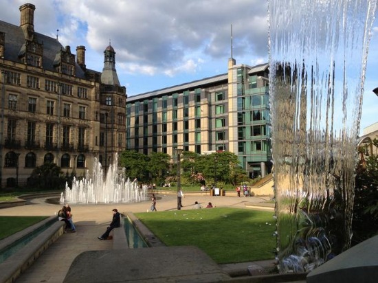 The fountain in front of Sheffield Town Hall, with people relaxing on the grass nearby, enjoying the sunny day.