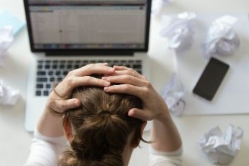 A woman holds her head in frustration while working intently at her laptop, indicating a busy workday.
