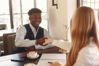 A employer and candidate shake hands at a table during a job interview.
