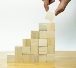 A person stacking wooden blocks on a wooden staircase, symbolizing progress and momentum after International Women's Day.