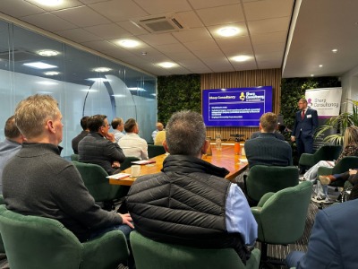 Andrew Walker presents an economic update at a roundtable discussion in a conference room, featuring Paul Mount from the Bank of England.