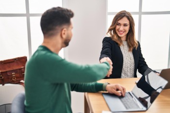 A woman and man shake hands at a desk, marking a job offer in finance and accountancy.