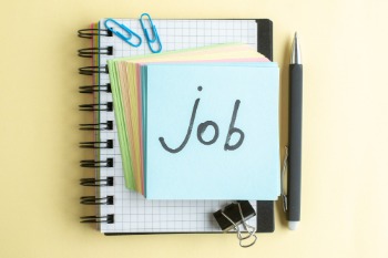 Job definition and description on a notebook with a pen and paper, set against a bright yellow background.