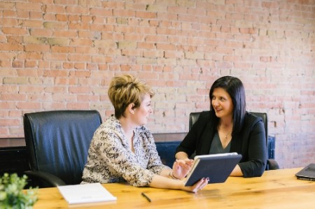 Two smartly dressed women in a modern office environment, one giving the other tips on her CV.