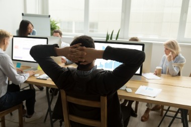 A man at a desk, hands behind his head, demonstrating a relaxed attitude towards workplace flexibility.