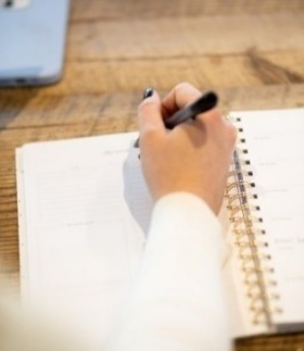 A woman focused on writing a cover letter in a notebook on a rustic wooden table.