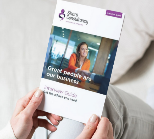 A person sat down holding a version of the Sharp Consultancy Interview guide, using the tips to complete a successful job interview.