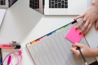 A person plans work conversations while typing on a laptop, with a notepad and pen beside them for notes.