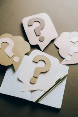 A notebook with question marks and a pen, resting on a rich brown surface, inviting curiosity and thought.