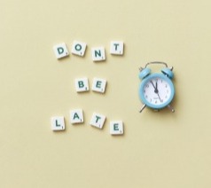 Scrabble letters spell "don't be late" beside an alarm clock on a bright yellow background.