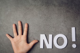 A hand making a "no" sign on a concrete surface, representing the concept of saying no in professional settings.