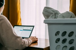An accountant working from home at a desk with a laptop, a basket of laundry beside them.