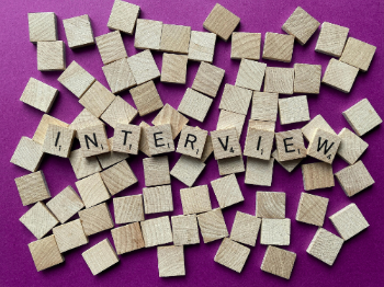 A bunch of wooden scrabble letters thrown onto a purple table with the word 'interview' shown.