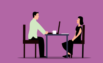A man interviewing a woman at a table, both focused on a laptop during a job interview.