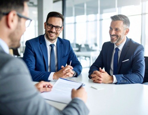 Three men smartly dressed in suits and ties, two interviewing the other for a job interview.