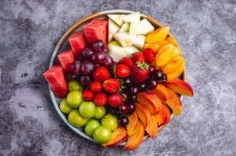 Fresh fruit platter featuring assorted fruits on a gray background, promoting healthy snacking at work.