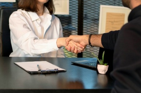 A man and woman shaking hands at a desk during a job interview for an accounting position.