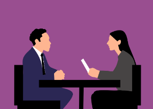 A man and woman sit at a table, engaged in conversation during a job interview for an accounting position.