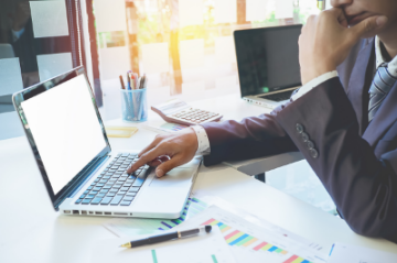  A man in a suit sits at a desk with a laptop, reviewing his Part Qualified finance CV.