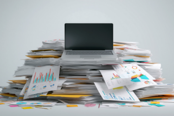 A laptop is placed atop a chaotic pile of papers, indicating a productive but cluttered environment.