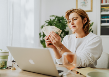 A woman sitting at a desk, holding money in her hand, symbolising her salary and financial success.
