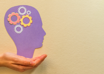 A person holds a paper cutout of a head filled with gears, symbolising thoughts or ideas in motion.