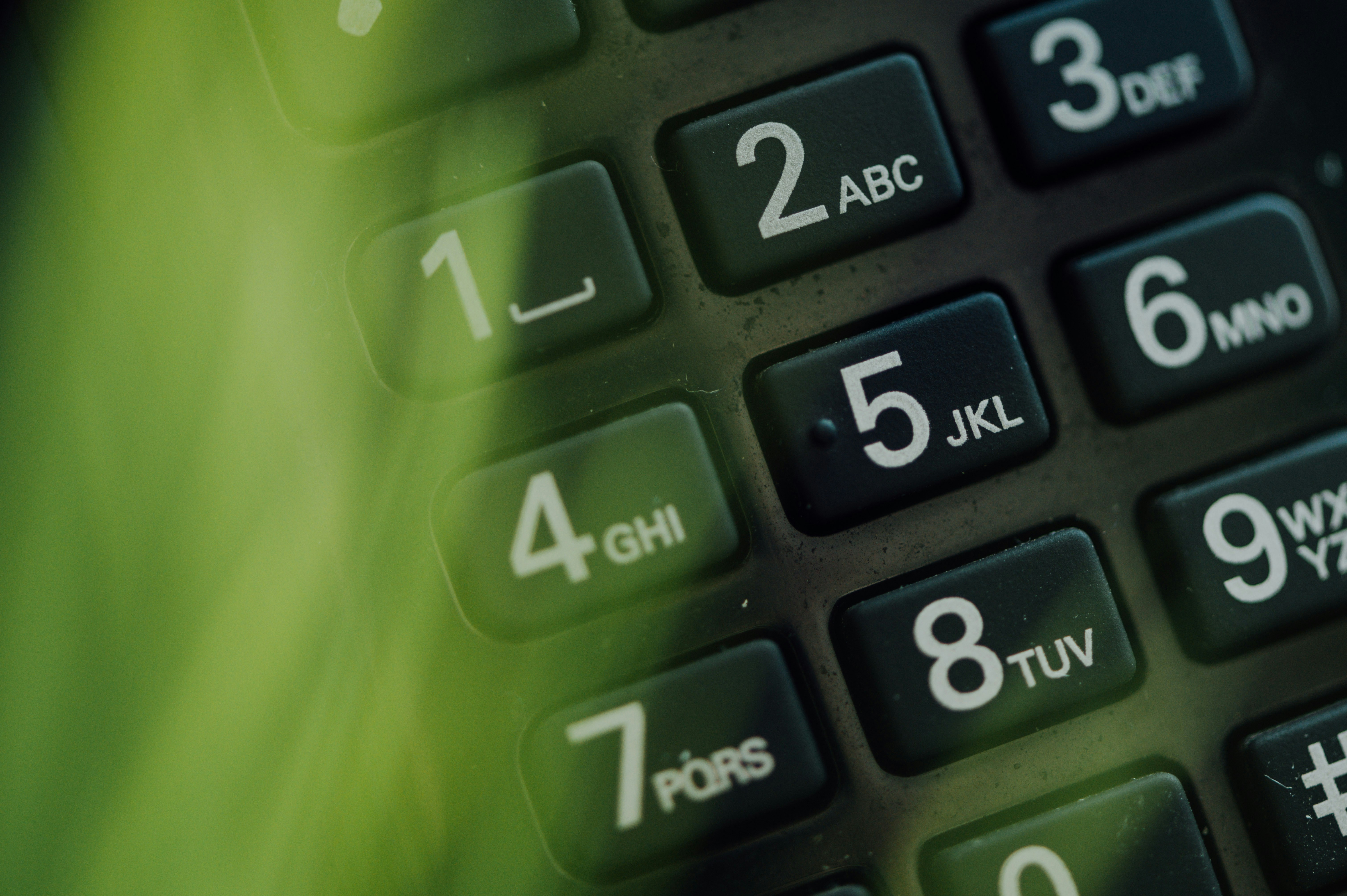 Close-up of a telephone keypad showing numbers and letters on black buttons. Soft green lighting adds a calm, focused atmosphere to the image.