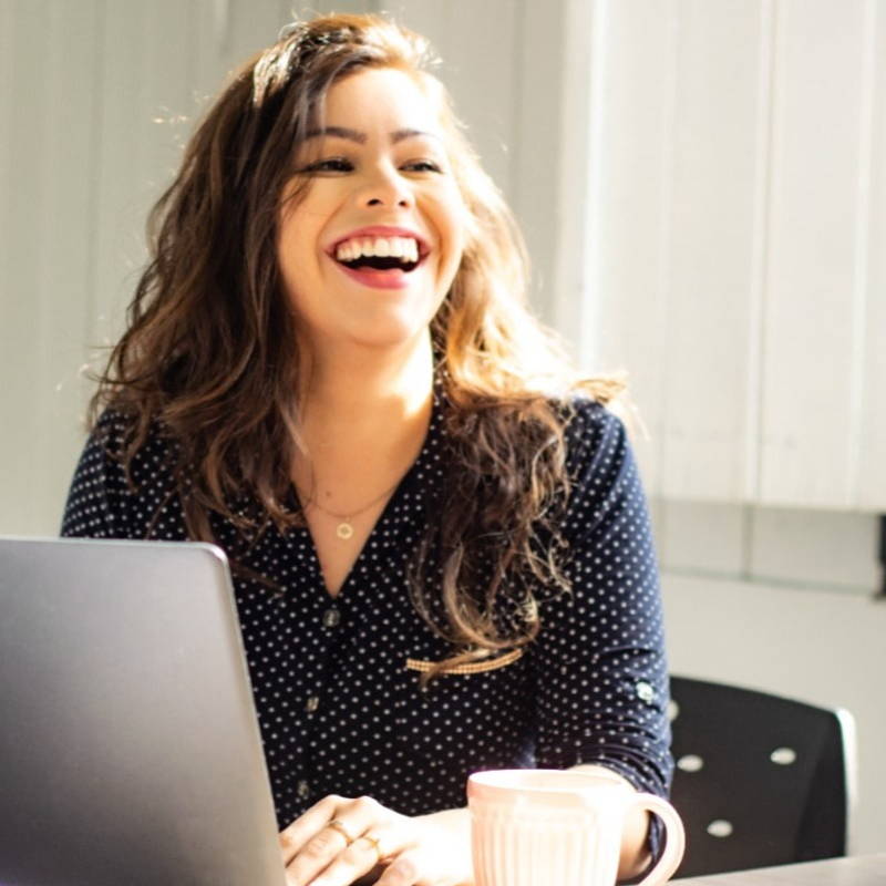 A professional female smiles as she sits at a laptop in a corporate office