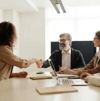 A businesswoman shakes hands with a panel during her second job interview, showcasing professionalism and confidence.