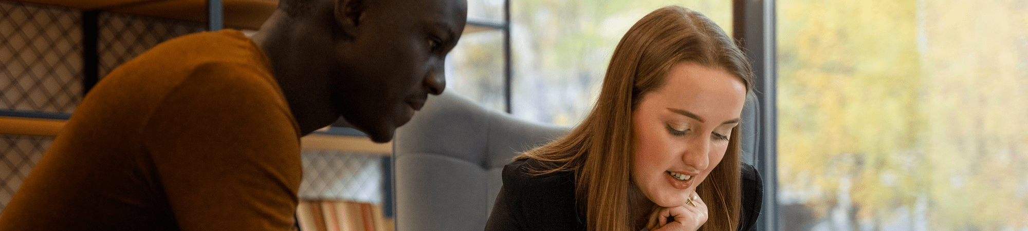 A woman and man at a table, discussing career advice for an accountancy and finance position while looking at a laptop.