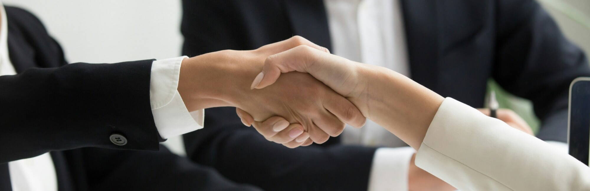 Two business professionals shake hands over a laptop during a job interview, symbolising agreement and collaboration.