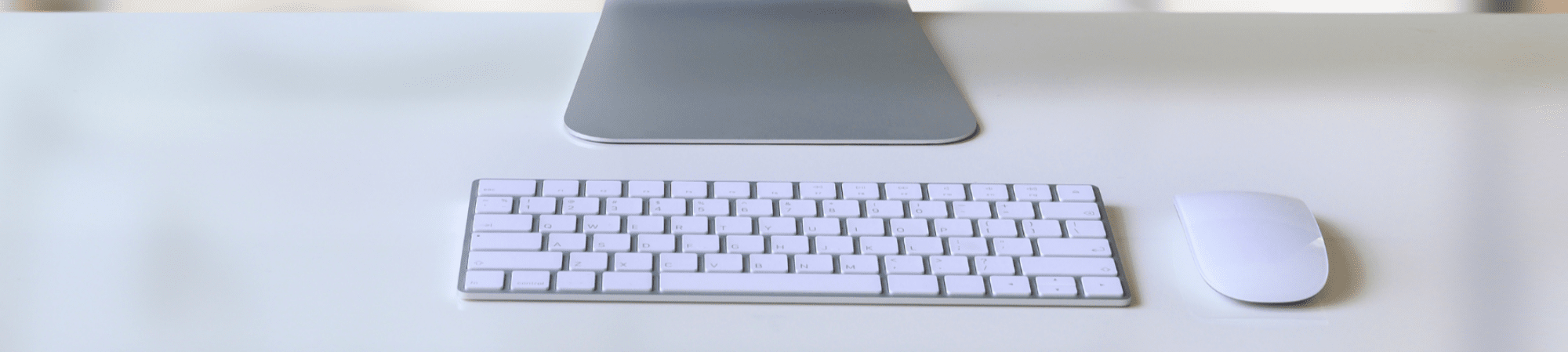 A silver and white computer keyboard and mouse on a tidy white desk.