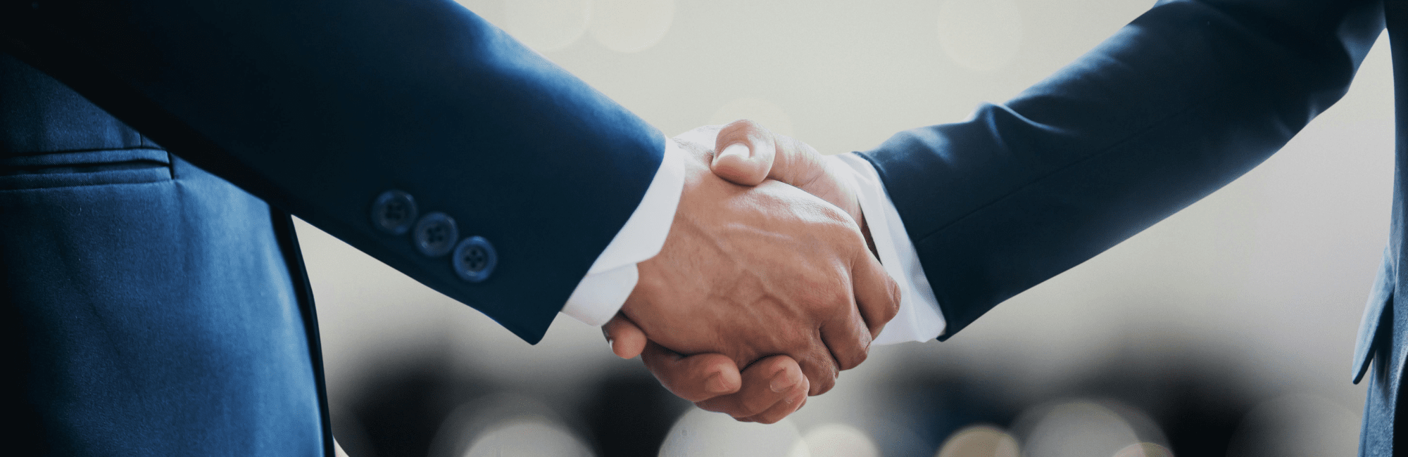 Two people in business suits shaking hands, shown in a close-up view, symbolizing agreement or partnership.