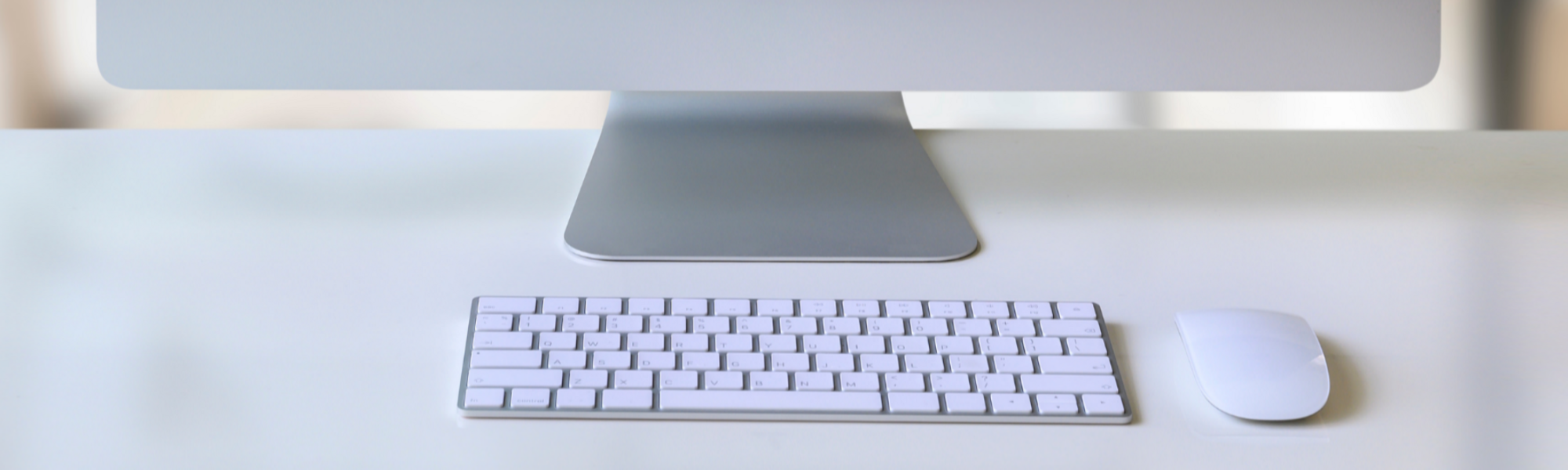 A silver and white computer keyboard and mouse on a tidy white desk.