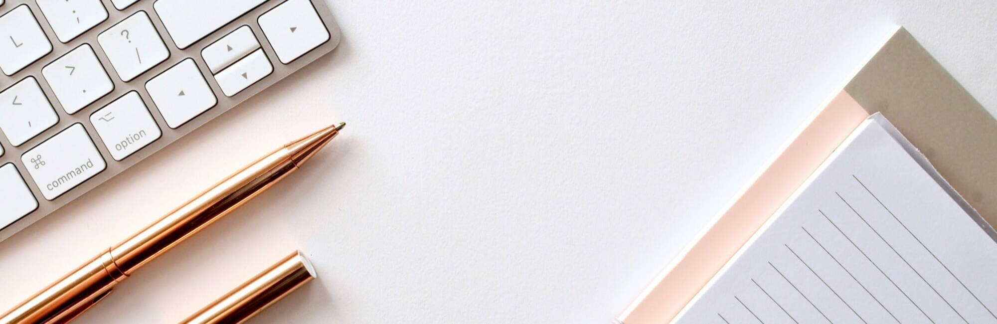 A white keyboard, a pair of round eyeglasses, two gold pens, a notepad, and a folder are arranged on a white desk—an organized setup ideal for accountancy or recruitment tasks.