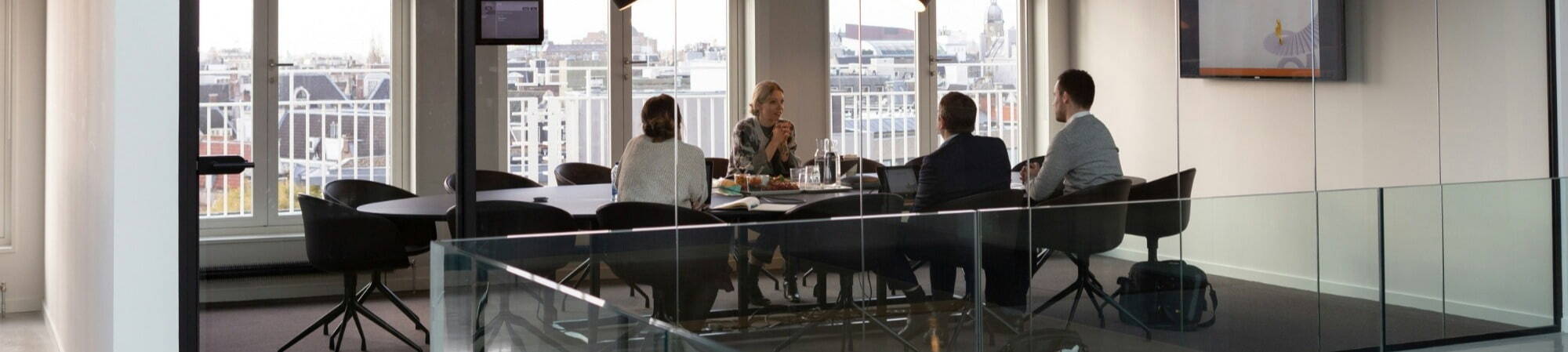 A glass-walled meeting room with a table and chairs, where a recruitment consultant meets with clients.