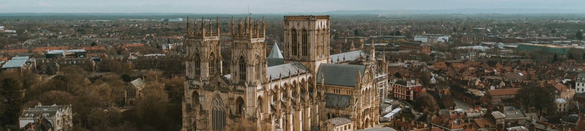 Aerial view of the York Minster surrounded by a charming medieval town. The cathedral's intricate Gothic architecture stands out against a backdrop of quaint red-roofed buildings.