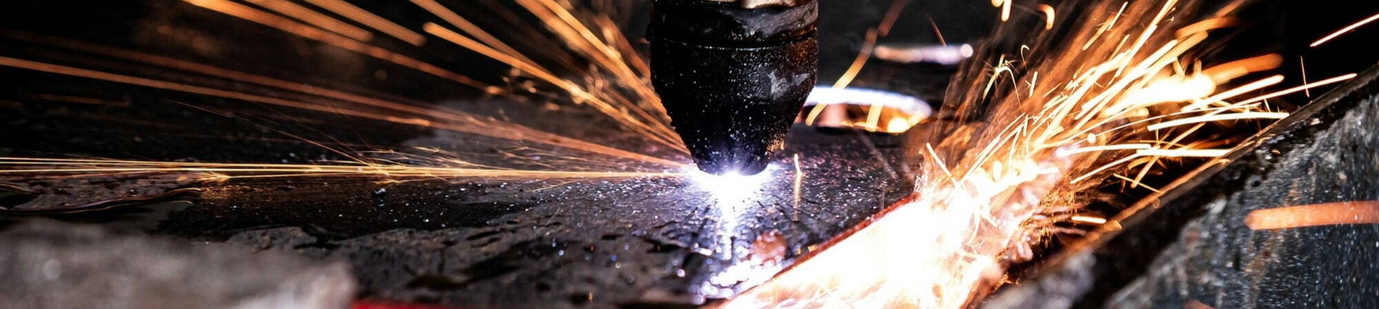 A welding machine is actively cutting metal, creating a shower of sparks that illuminate the workspace.