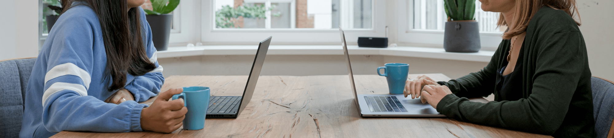Two women at a table with laptops, one a recruitment consultant assisting the other with CV improvements for finance and accountancy jobs.