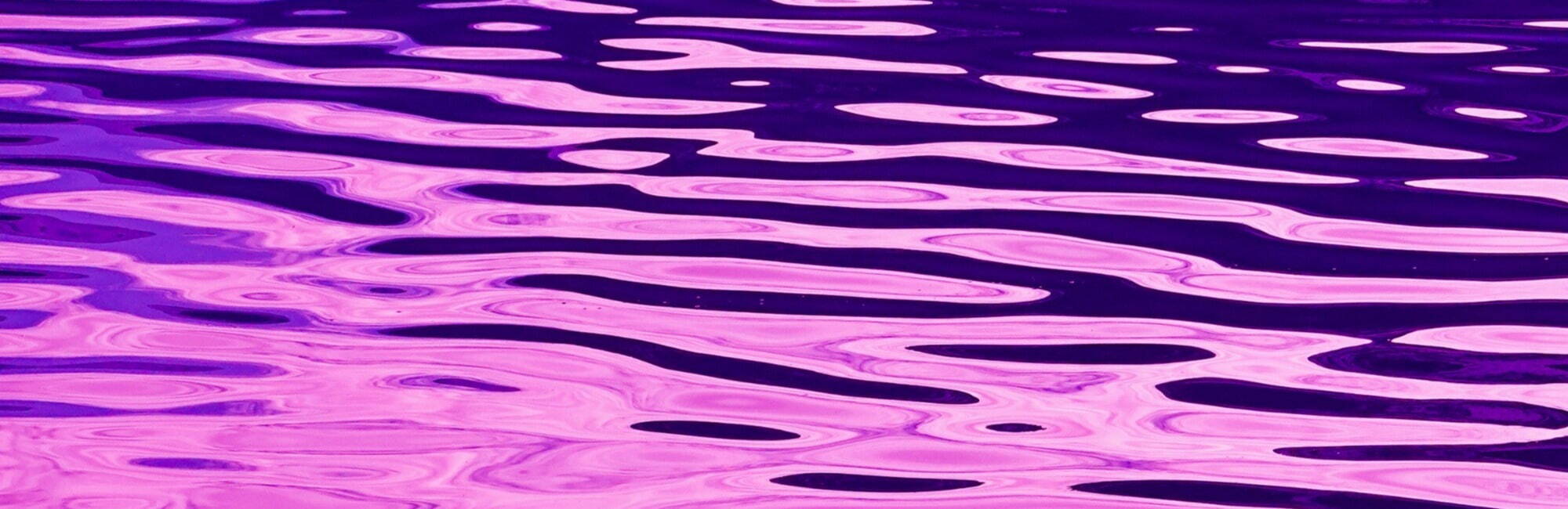 A tranquil scene of rippling water, blending purple and pink hues, evoking a peaceful and dreamy atmosphere.
